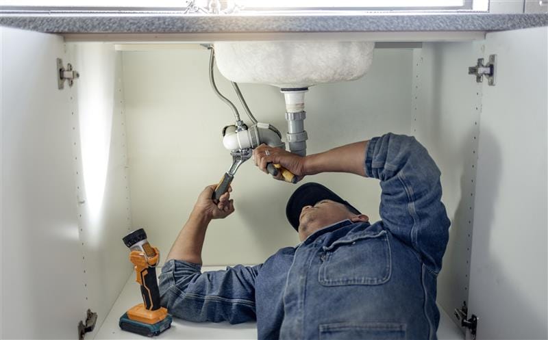 Plumber repairing pipes beneath a bathroom sink in Apopka