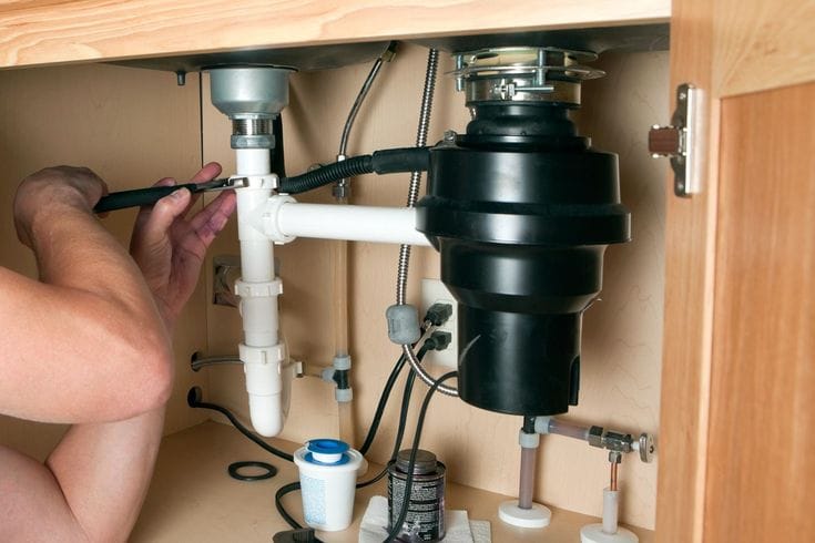 Plumber installing a garbage disposal beneath a kitchen sink in Apopka
