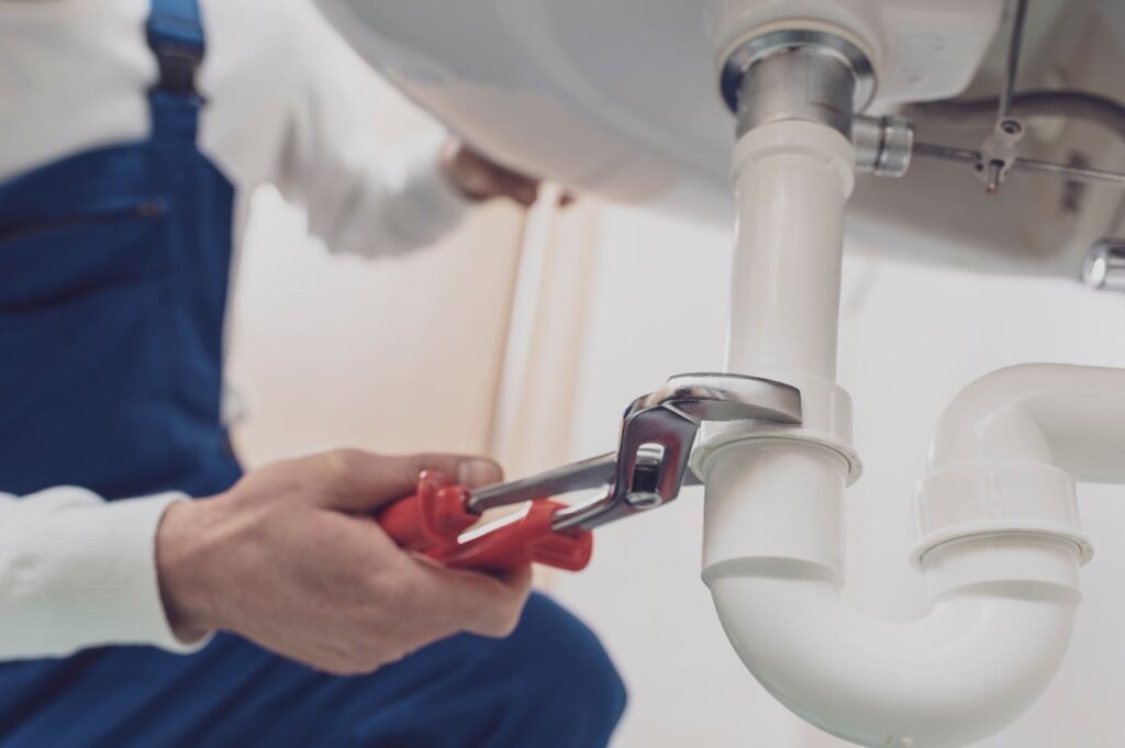 Plumber repairing a white drain pipe beneath a sink in Apopka